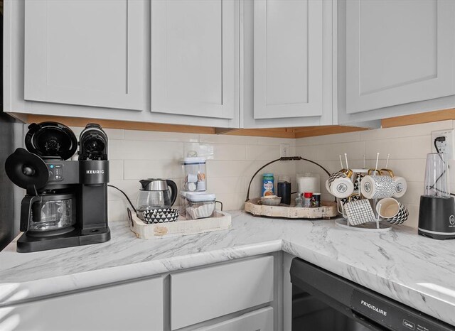 interior space featuring decorative backsplash, black dishwasher, white cabinetry, and light stone countertops