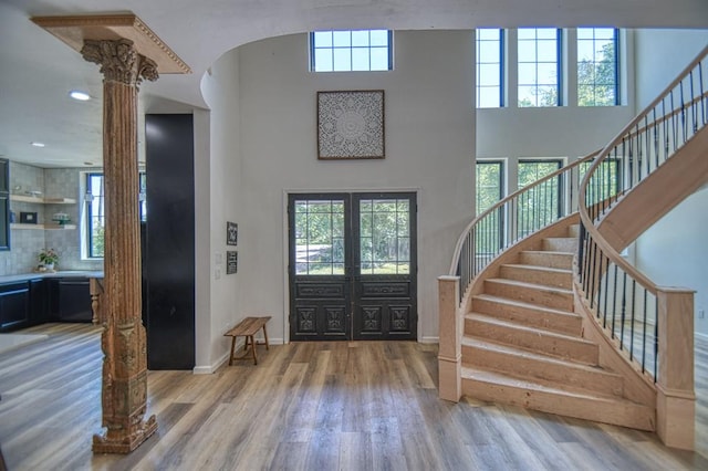 foyer featuring french doors, ornate columns, a towering ceiling, and light wood-type flooring