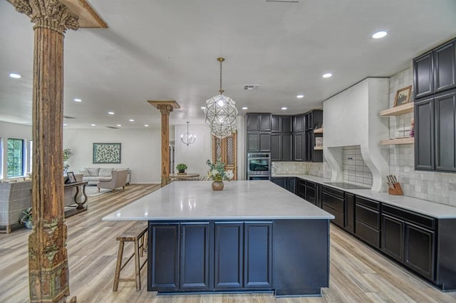 kitchen featuring a large island, decorative columns, light hardwood / wood-style floors, decorative backsplash, and decorative light fixtures