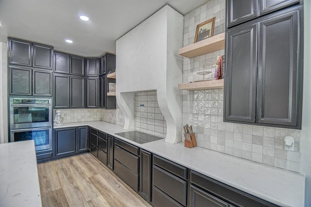 kitchen featuring tasteful backsplash, black electric stovetop, light stone countertops, stainless steel double oven, and light hardwood / wood-style flooring