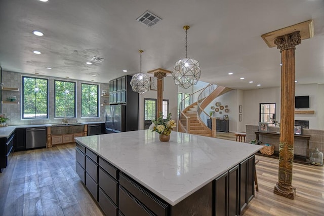 kitchen with appliances with stainless steel finishes, hanging light fixtures, a center island, light stone countertops, and ornate columns