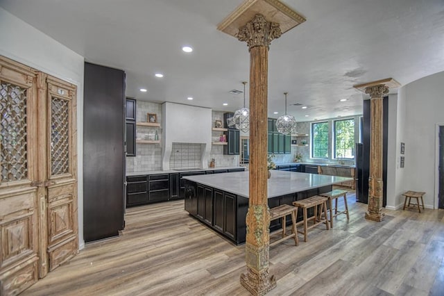 kitchen with ornate columns, tasteful backsplash, a kitchen island, and light hardwood / wood-style flooring