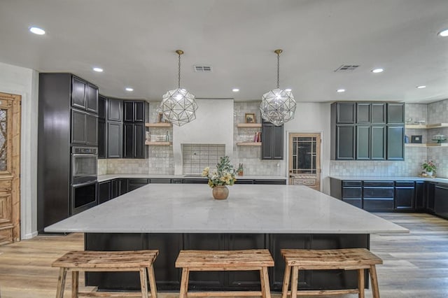 kitchen with hanging light fixtures, light stone countertops, a large island, and light hardwood / wood-style flooring