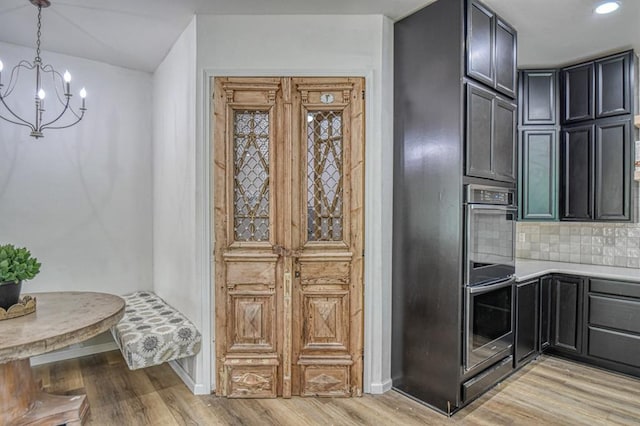 kitchen featuring an inviting chandelier, decorative light fixtures, stainless steel double oven, light hardwood / wood-style floors, and backsplash