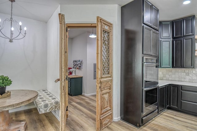 kitchen featuring pendant lighting, double oven, backsplash, a notable chandelier, and light hardwood / wood-style floors