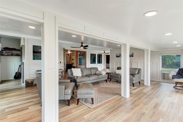 living room with light wood finished floors, ceiling fan, and a decorative wall