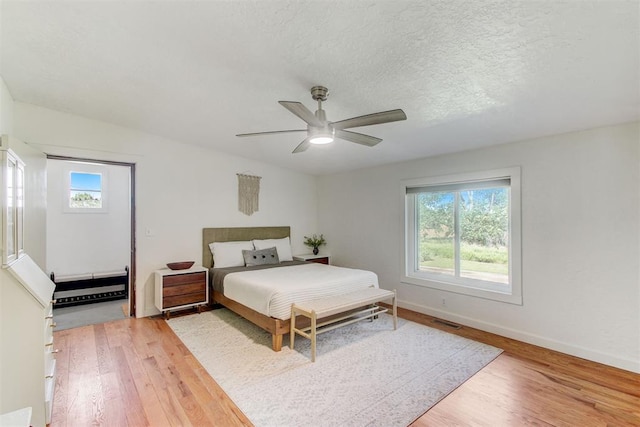 bedroom featuring light wood-type flooring, visible vents, a textured ceiling, and multiple windows