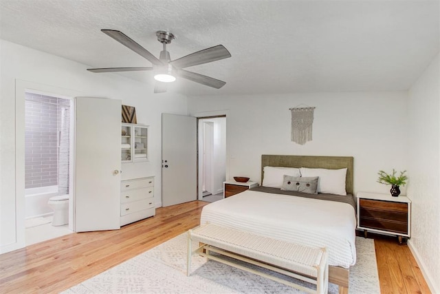 bedroom with light wood-style floors, ensuite bath, a ceiling fan, and a textured ceiling