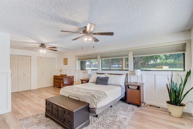 bedroom with light wood finished floors, a textured ceiling, a decorative wall, and two closets