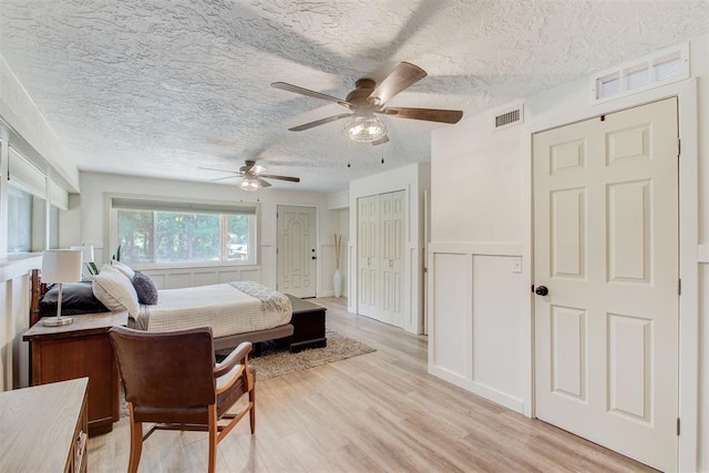 bedroom with visible vents, a textured ceiling, light wood-type flooring, a decorative wall, and multiple closets