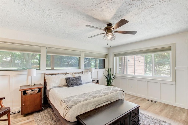 bedroom with a textured ceiling, a decorative wall, a ceiling fan, visible vents, and light wood-type flooring