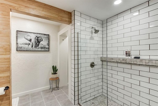 bathroom with a tile shower, baseboards, and tile patterned floors