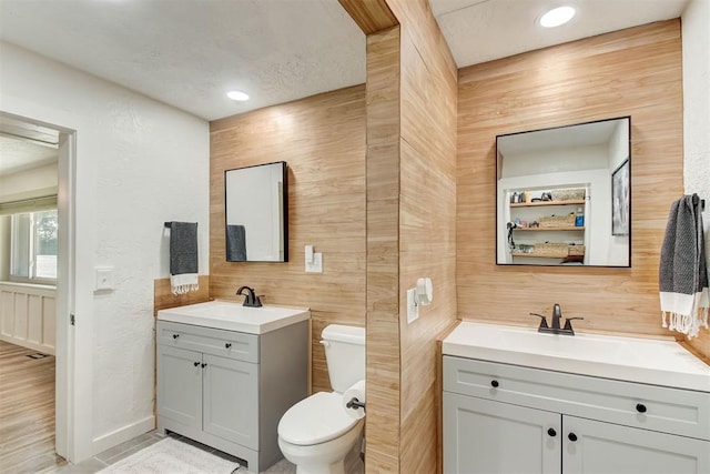 bathroom featuring two vanities, a sink, toilet, and wooden walls