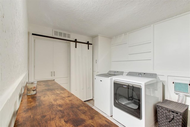 laundry area featuring a textured ceiling, a barn door, laundry area, visible vents, and independent washer and dryer