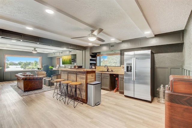 kitchen with a breakfast bar, light wood finished floors, a sink, a textured ceiling, and stainless steel fridge with ice dispenser