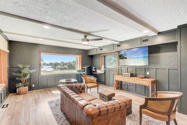 living room with visible vents, a decorative wall, light wood-style floors, a textured ceiling, and beamed ceiling