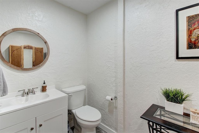 bathroom with a textured wall, vanity, and toilet