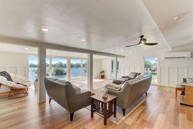 living room featuring a wall unit AC, light wood-style flooring, a water view, a textured ceiling, and a decorative wall