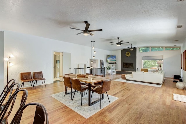 dining area featuring a textured ceiling, light wood-style flooring, a fireplace, and visible vents