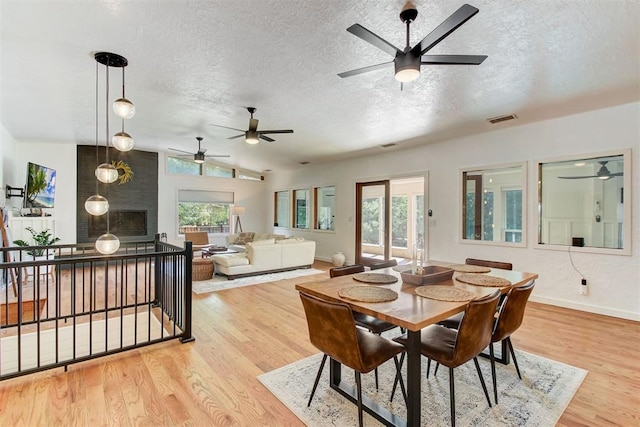 dining area with a textured ceiling, vaulted ceiling, wood finished floors, and visible vents