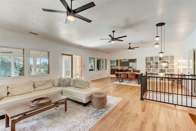 living area featuring lofted ceiling, light wood-style floors, visible vents, and a textured ceiling