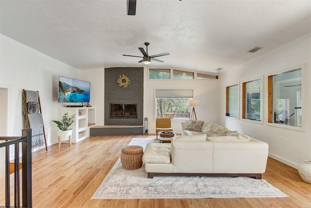 living room with a fireplace, light wood finished floors, lofted ceiling, visible vents, and a textured ceiling