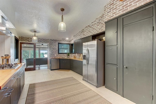 kitchen featuring light tile patterned floors, brick wall, appliances with stainless steel finishes, hanging light fixtures, and a textured ceiling