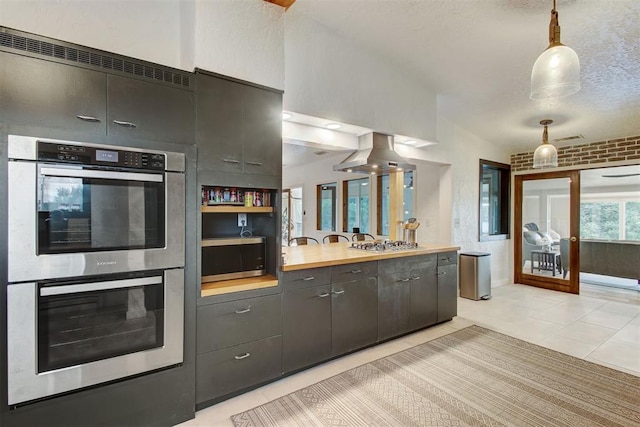 kitchen with island range hood, wood counters, stainless steel appliances, pendant lighting, and light tile patterned flooring