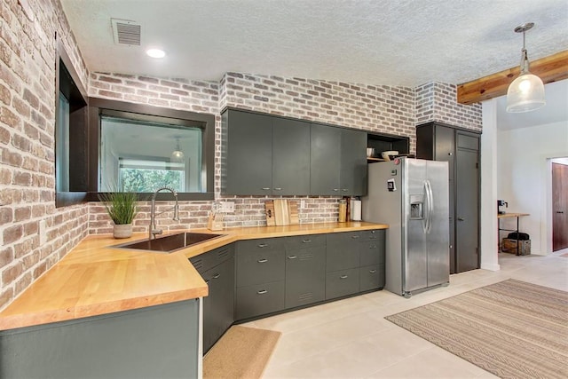 kitchen featuring brick wall, stainless steel refrigerator with ice dispenser, a sink, and visible vents