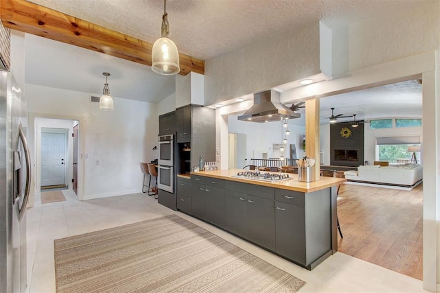 kitchen featuring a large fireplace, a ceiling fan, appliances with stainless steel finishes, ventilation hood, and beam ceiling