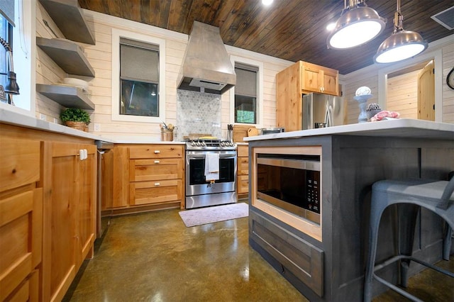 kitchen featuring stainless steel appliances, wall chimney range hood, a kitchen breakfast bar, decorative light fixtures, and wooden walls