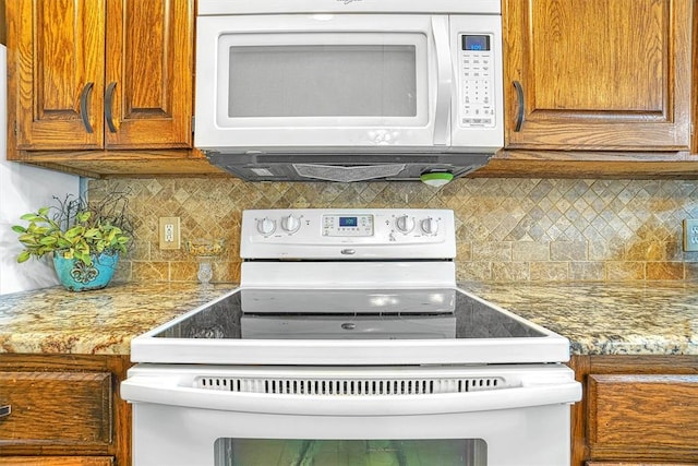 kitchen featuring backsplash, light stone countertops, and white appliances