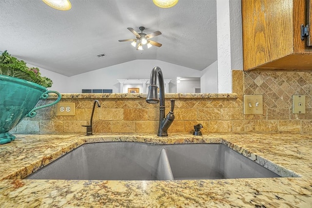 kitchen with ceiling fan, sink, backsplash, a textured ceiling, and lofted ceiling