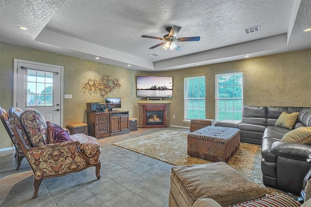 tiled living room with a textured ceiling, a tray ceiling, and ceiling fan