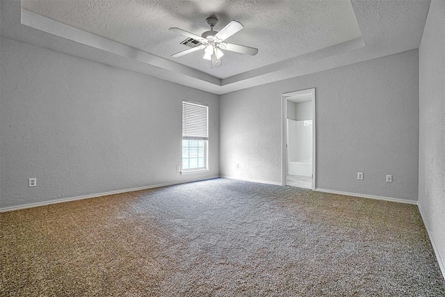 empty room with a textured ceiling, carpet floors, a raised ceiling, and ceiling fan