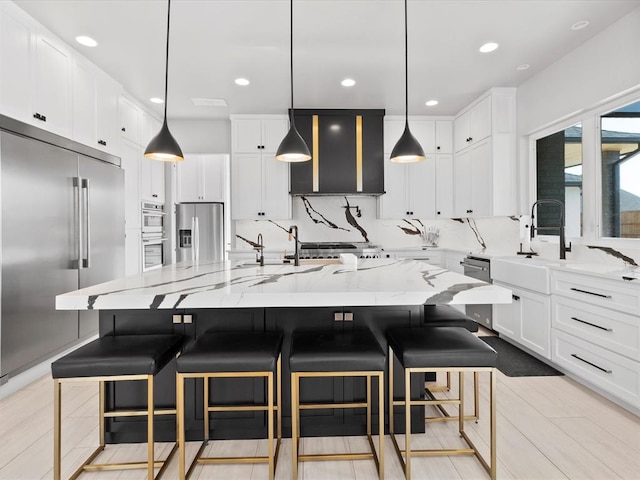 kitchen featuring pendant lighting, a breakfast bar, a large island with sink, white cabinets, and appliances with stainless steel finishes