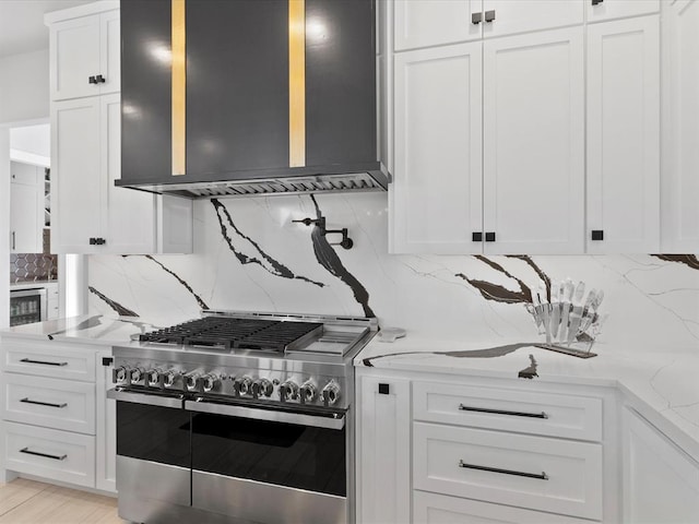 kitchen with wall chimney range hood, backsplash, white cabinets, and high end stainless steel range oven