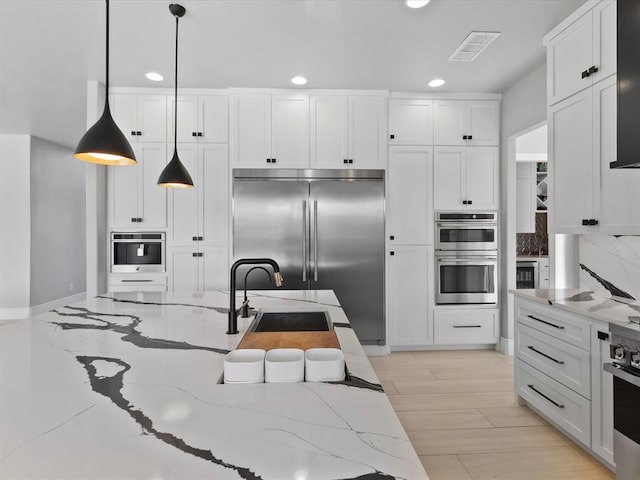 kitchen featuring white cabinets, sink, hanging light fixtures, appliances with stainless steel finishes, and light stone counters