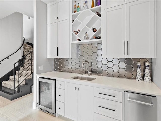 kitchen featuring sink, beverage cooler, tasteful backsplash, stainless steel dishwasher, and white cabinets