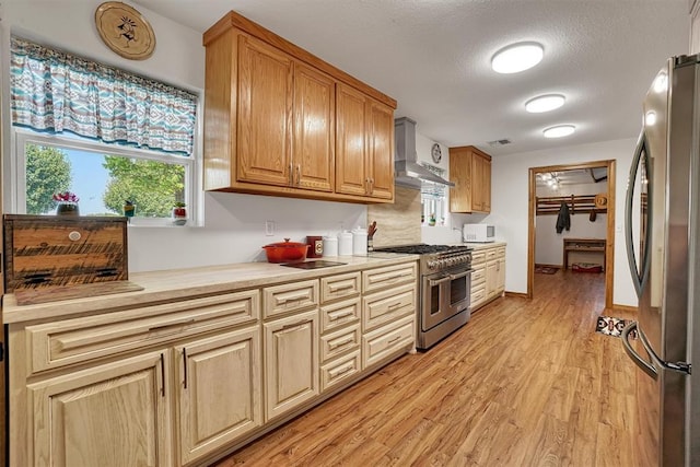 kitchen featuring appliances with stainless steel finishes, a textured ceiling, light hardwood / wood-style floors, and wall chimney range hood