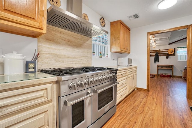 kitchen featuring light brown cabinetry, light hardwood / wood-style floors, range with two ovens, and wall chimney range hood