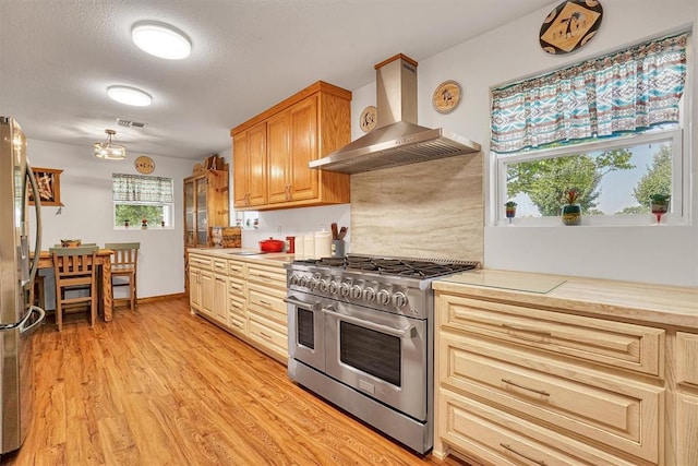 kitchen with a textured ceiling, light wood-type flooring, wall chimney range hood, and appliances with stainless steel finishes