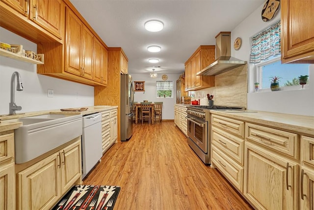 kitchen featuring sink, stainless steel appliances, wall chimney range hood, and light hardwood / wood-style flooring