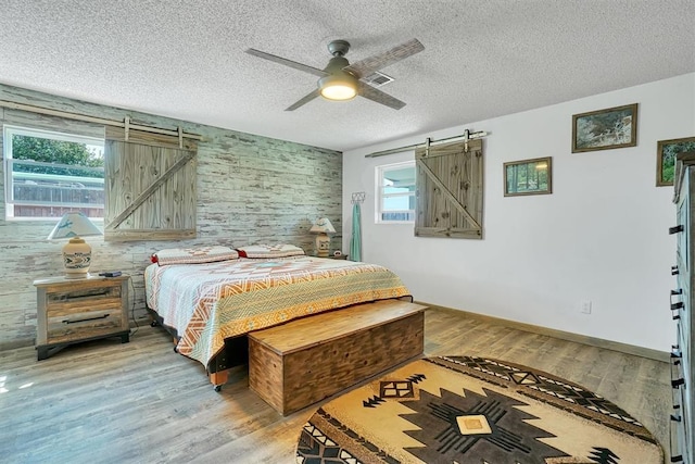 bedroom with hardwood / wood-style flooring, ceiling fan, a barn door, and a textured ceiling