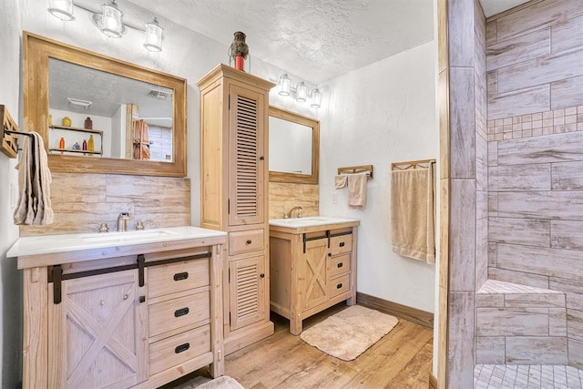 bathroom with vanity, hardwood / wood-style flooring, decorative backsplash, tiled shower, and a textured ceiling