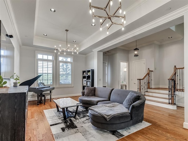 living room featuring a chandelier, light wood-type flooring, ornamental molding, and a tray ceiling