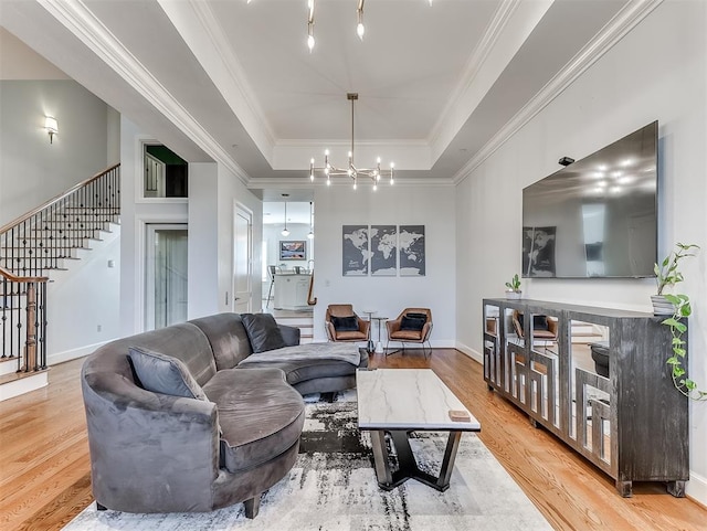 living room featuring a notable chandelier, crown molding, a tray ceiling, and light hardwood / wood-style flooring