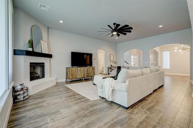 living room with a brick fireplace, ceiling fan with notable chandelier, and light hardwood / wood-style flooring