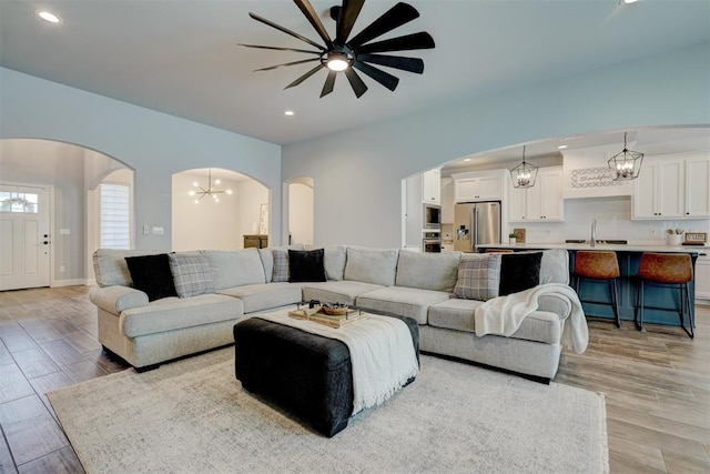 living room featuring ceiling fan with notable chandelier, light hardwood / wood-style floors, and sink