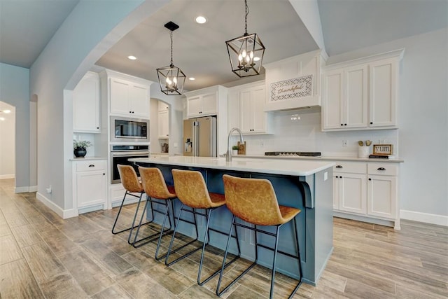 kitchen featuring an inviting chandelier, white cabinets, light wood-type flooring, an island with sink, and stainless steel appliances